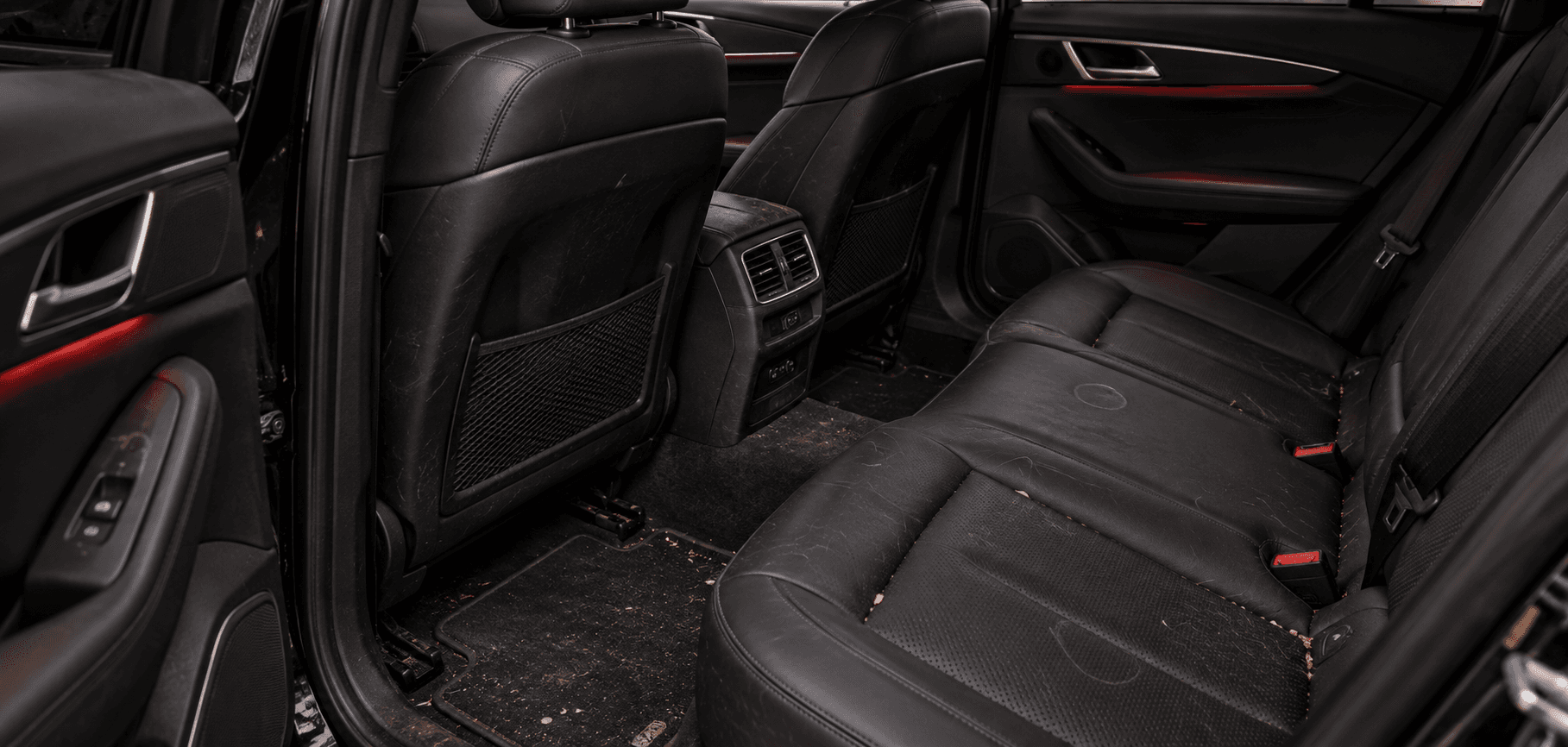 Rear seats and floor mats of a car before detailing, covered in dirt and debris
